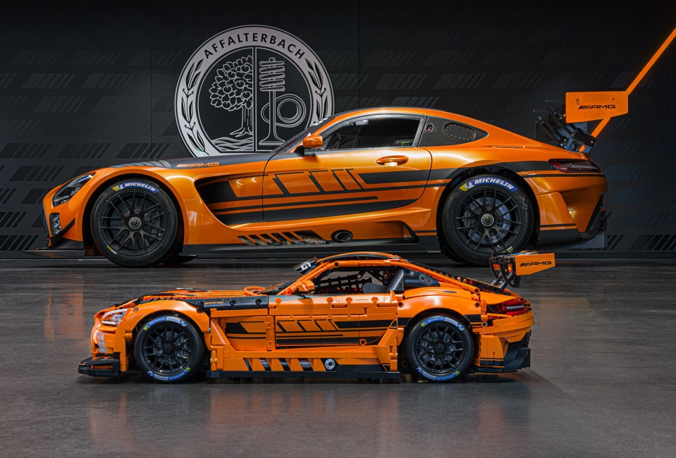 Zu sehen ist das Mercedes-AMG GT3 Klemmbaustein Modell in orange zusammengebaut. Es steht vor vor einem Hintergrund mit einem Foto des GT3 und AMG Logo auf schwarzem Hintergrund.