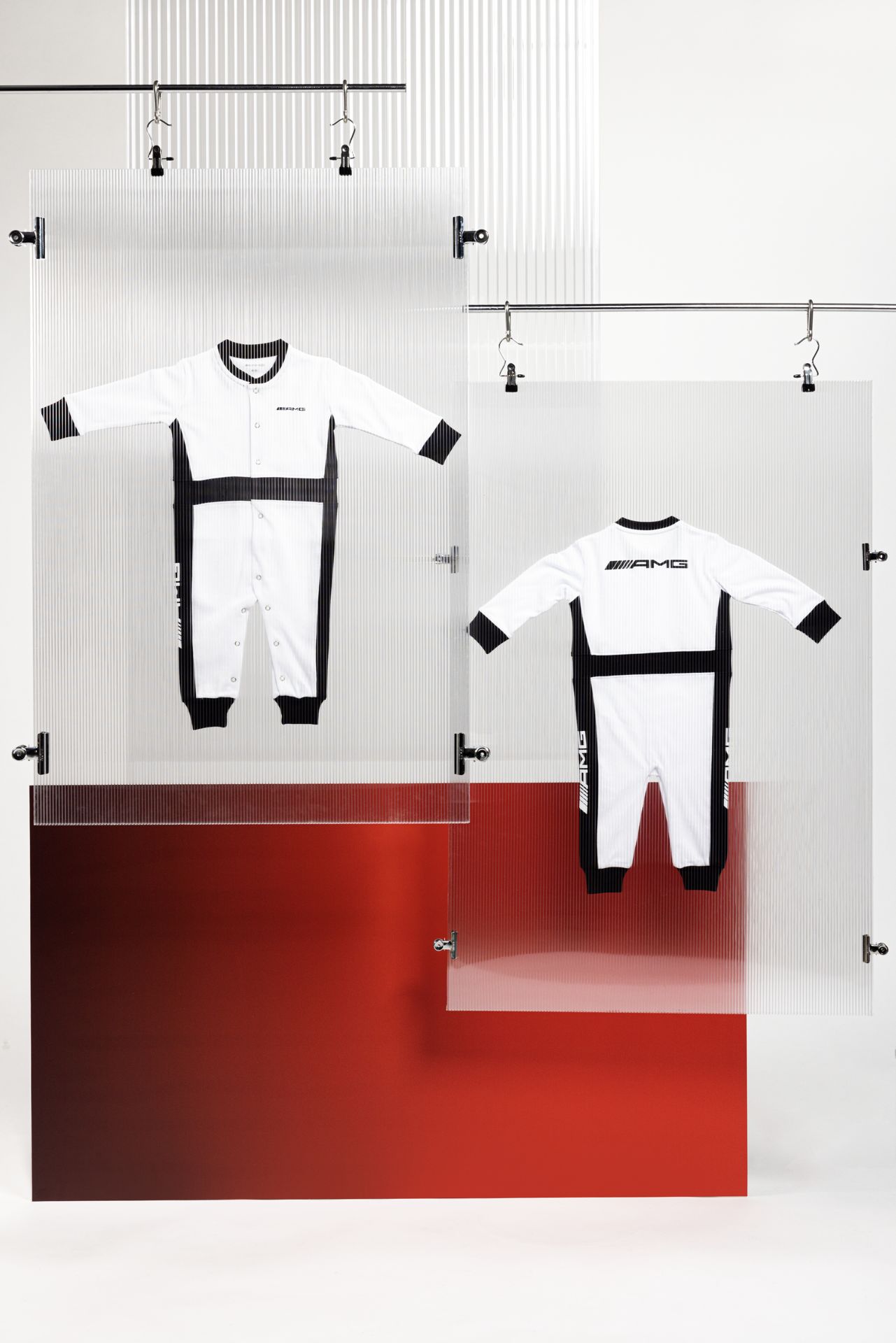 Zwei Babystrampler B66959635 von AMG, schwarz-weiß, aufgehängt an einer Kleinerstange. Verlinkt auf die Kategorie: Mode_Kids