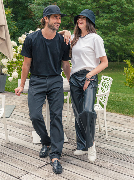 Abgebildet sind ein Mann und eine Frau. Beide sind schwarz / weiß in der Mercedes-Benz Mode Kollektion gekleidet. Sie stehen auf einer Terasse vor grünem Hintergrund.